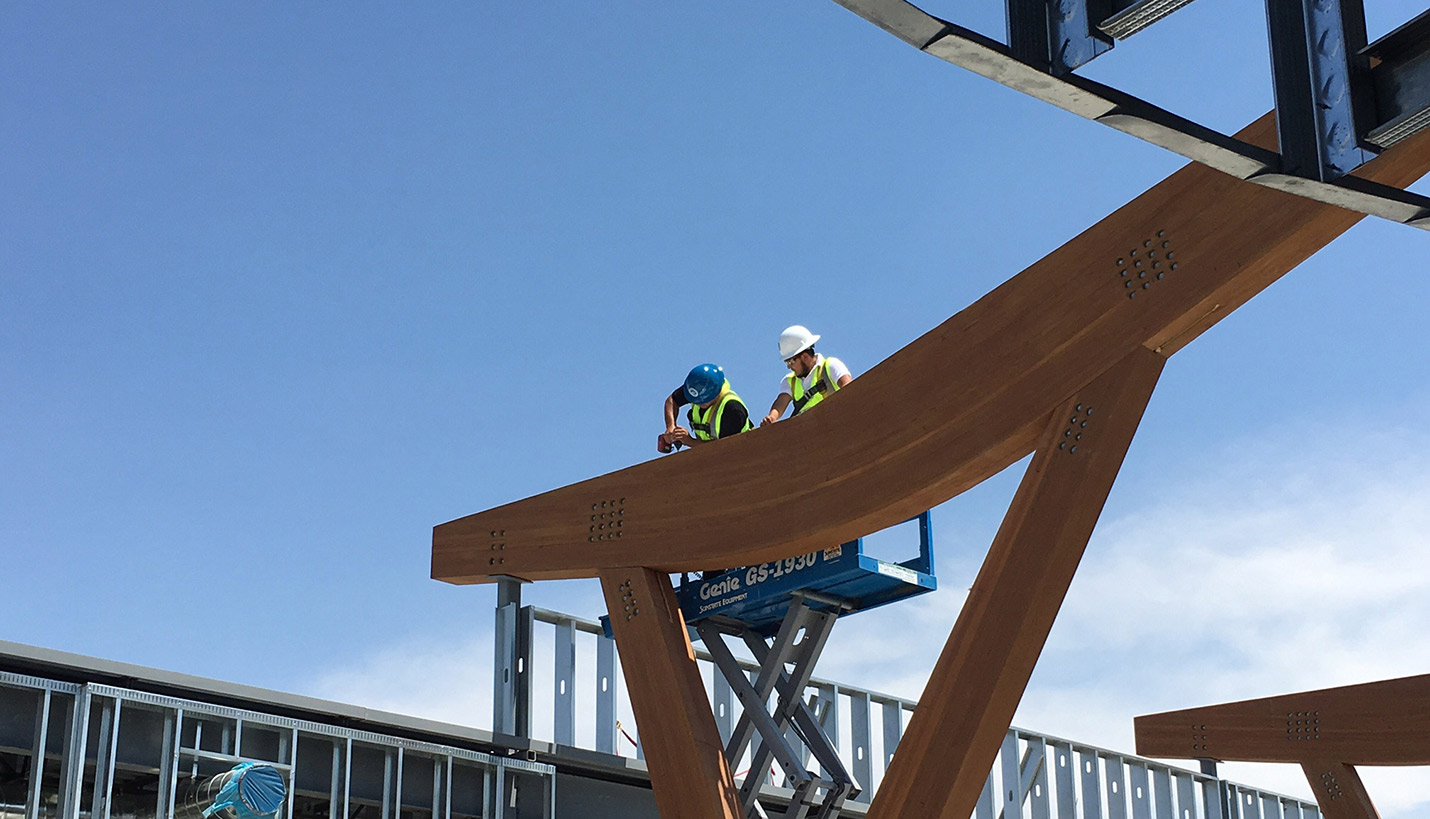 Workers drill a ceremonial plate signed by all project team members against a structural beam. The act, known as topping out, signifies a project milestone. - Page